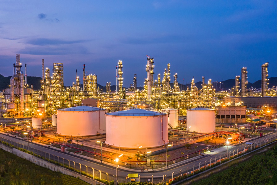 Oil storage tank with refinery in the back at night
